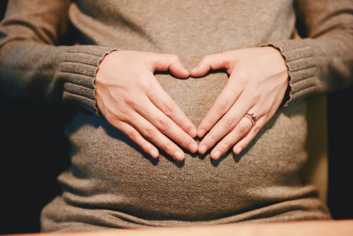 Schwangere hält ihre Hände in Herzform vor ihren Bauch